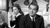 A woman in a black dress sits on a bed with a cigarette, looking away, as a man in a suit sits pensively nearby—an evocative black-and-white scene reminiscent of The Rise and Fall of Legs Diamond (1960) DVD.