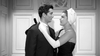 A woman in a dark dress and white gloves embraces a man in a suit by a decorative white wall, echoing iconic moments from "The Rise and Fall of Legs Diamond (1960) DVD.