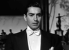 A man in a black tuxedo and white bow tie stands indoors with a serious, film noir expression, evoking the timeless black-and-white mood of "Nightmare Alley (1947) DVD," enhanced by blurred statues and shadows in the background.