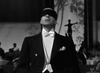 A man in formal evening wear with a black blindfold stands center stage, echoing film noir mystery. Blurred figures and a shadowy form loom behind him—capturing the intrigue of Nightmare Alley (1947) DVD.