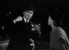 A man in a dark suit and hat raises his fists to fight a woman in a coat and hat against a nighttime backdrop—a dramatic moment from Nightmare Alley (1947) DVD.