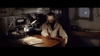 A man in a beige jacket sits at a cluttered desk aiming a gun, surrounded by office supplies and equipment, evoking the suspense of "When Eight Bells Toll (1971)" on DVD.