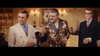 Three men in suits stand in an elegantly lit room; the one in the center, wearing a brown patterned jacket and holding a drink, gestures as others listen—reminiscent of scenes from "When Eight Bells Toll (1971)" on DVD, with ornate decor and lamps behind them.