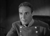 A man in a military-style uniform with double rows of buttons sits indoors, reminiscent of scenes from the black-and-white classic, Virginia City (1940) DVD.