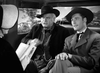 Two men in cowboy hats sit in a stagecoach, talking to a woman reading from a book—a scene from the classic Civil War film Virginia City (1940), starring Errol Flynn, available on DVD.