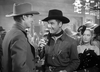 Two men in cowboy hats chat at a lively bar while a woman in a feathered hat stands nearby, capturing the classic Civil War-era style seen in the black-and-white film "Virginia City (1940)"—now available on DVD.