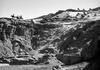 A group of riders on horseback descends a rocky desert slope under a clear sky, evoking scenes from the classic film Virginia City (1940) DVD with its steep cliffs and rugged terrain.