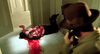 A sheriff in a brown hat talks on the phone, surveying a crime scene with a wounded man in blood, echoing the tense drama of The Public Eye DVD (1992), with splattered walls and a brightly lit hallway.