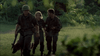 Three people in military uniforms walk through green foliage, one leading with a helmet and a German Shepherd. This scene, reminiscent of wartime camaraderie, is captured in the film "Rain (2006)" available on DVD.