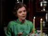 A woman in a green blouse sits at a table with two lit candles, speaking or gesturing; shelves in the background hold silver items and the "Father Knows Best Reunion (1977) DVD.