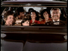 Four adults and two children sit closely in the front seat of a vintage car, all smiling joyfully—just like a scene from the "Father Knows Best Reunion (1977) DVD.