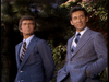 Two men in gray suits and striped ties stand outdoors before greenery, looking right—like they’re discussing the "Father Knows Best Reunion (1977)" DVD. One has hands in his pockets; the other’s arms rest at his sides.