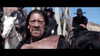 A rugged man with long dark hair and weathered skin stands in front, holding leather, as men in dark hats sit on horses beneath a blue sky—evoking scenes from rare DVDs like The Ridiculous 6 (2015) comedy starring Adam Sandler.