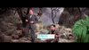 Two men in suits are outdoors among rocks and dry grass; one holds a small item, while the other examines a colorful map—perhaps planning a trip to find rare films like the Brigadoon (1954) DVD. A backpack and hat lie under a nearby tree.