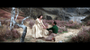 A woman in a cream dress stands holding hands with a kneeling man in a grassy, scenic landscape with purple flowers, trees, and hills—evoking the romantic charm of "Brigadoon (1954)" on DVD.