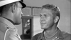 Two men talk indoors—one in a military uniform with cap faces away, the other in a jacket and turtleneck smiles slightly, evoking classic scenes found on the "Soldier in the Rain (1963) DVD.
