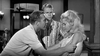 A tense black and white scene indoors recalls classic movies like Soldier in the Rain (1963) DVD, as a man in a short-sleeved shirt grabs a blonde woman's arm while she looks down, upset, and another man stands between them looking concerned.