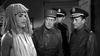 A person in a sheet and mop wig faces three stern men in military uniforms in a dim room—an unusual scene echoing classic films like Soldier in the Rain (1963) on DVD.