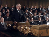 An older man in a suit speaks passionately at a podium before an audience in a grand chamber adorned with gold objects, capturing the tense diplomacy of WWII as shown in "Countdown to War (1989)" on DVD.