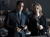 A suited man and a woman in a dark jacket stand together in a courtroom, with people seated behind them and papers on the table—capturing the dramatic intensity of "Obsessed (2002)" DVD.