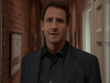 A man with short brown hair in a dark suit stands in a hallway with exposed brick walls and framed pictures, evoking the atmosphere of a true-crime drama like the Obsessed (2002) DVD cover.