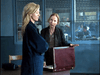 Two women stand in an office, one facing forward with arms crossed and the other gesturing to an open briefcase—echoing the suspense of a true-crime drama. A barred window hints at mystery in this scene from Obsessed (2002) DVD.