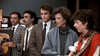 Five people in 1980s-style outfits stand indoors, evoking a classic film vibe. Three men in suits and two women—one with a guitar—pose before a photo board, representing the "Nothing in Common (1986) DVD.