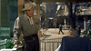 A man in cowboy attire chats with an older man on a western town porch, surrounded by wooden buildings and a picket fence—a scene straight from The Bounty Hunter (1954) DVD.