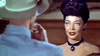 A dark-haired woman in an updo and black choker faces forward, speaking to a man in a hat with his back to the camera—a vintage scene evoking bounty hunter western classics like The Bounty Hunter (1954) DVD.