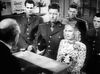 A woman in a patterned dress with a bow sits at a counter, four uniformed men behind her and an older man across—like a classic wartime musical. Watch this scene in Stage Door Canteen (1943) DVD, now available.