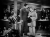 A black-and-white scene from the "Stage Door Canteen (1943) DVD" shows a crowded room with a woman on the left and two men—one in military uniform, one in a suit with bowtie and cane—capturing classic film charm.