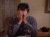 A person sits at a table, face in hands, looking frustrated—a scene evoking family drama like that in "Promise (1986)" DVD. A glass of water and a plate are on the table in the softly lit room.