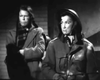 Two people in winter coats and head coverings stand closely together indoors, looking serious. The dramatic black and white lighting recalls classic wartime films like Guerrilla Girl (1953) DVD.