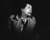 A man in a trench coat and tie looks anxiously to his right, mirroring the suspenseful tension of wartime dramas like Guerrilla Girl (1953) DVD, inspired by classic film noir masterpieces.