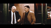 Two older men, one in a black suit and tie with gray hair, the other in a tan blazer with curly hair, talk outside at night before dark doors and brown stone—like a scene from "The Caller (2008)" DVD.