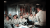 A group of men in khaki uniforms sit in rows, listening to an instructor, echoing a classic military scene from the "Flat Top (1952) DVD," with life jackets hanging on the walls reminiscent of a Korean War drama.