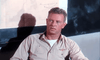 A man with short curly hair in a khaki shirt and winged badge sits by a chalkboard, evoking the tension found in classic war films like Flat Top (1952) DVD.