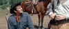 A cowboy in a dark hat and red neckerchief looks up at another, with a saddled brown horse behind—capturing the timeless western spirit of "These Thousand Hills (1959)" now on DVD.