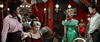 A lively saloon scene from "These Thousand Hills (1959) DVD" features people in Western attire—a woman in a bright green dress near a cowboy-hatted man, and another woman seated at a table amid red walls, lamps, and chandeliers.