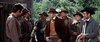 A tense standoff unfolds outdoors as men in cowboy attire face off in "These Thousand Hills (1959)" on DVD, with one holding a rifle and a wooden building and trees visible in the background, echoing classic American western scenes.