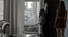 A man in a suit greets a woman in a red skirt at the door of a modern apartment, city buildings behind them. A subtitle says: Hi, Patrick. This scene is reminiscent of those found in rare movies like the Nelly (2016) DVD.
