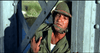 A soldier in green uniform and helmet leans against a metal structure, wounded and grimacing—capturing the tense WWII action from Legion of No Return (1969) DVD, with greenery and water in the background.