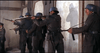 A squad of five soldiers in dark uniforms and blue helmets aims rifles against a weathered wall in this intense WWII scene from the "Legion of No Return (1969)" DVD, with sunlight casting dramatic shadows behind them.
