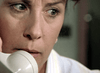 Close-up of a fair-skinned, light-eyed woman holding a phone receiver, looking tense as if hearing chilling news—a gripping scene from "The Investigation (2002)" DVD.