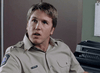 A man in a khaki police uniform sits indoors with a surprised or attentive expression by a typewriter and clipboard—a scene from "The Investigation (2002) DVD," perfect for rare movie or true crime DVD collectors.