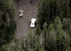A white vehicle with open doors is parked on a dirt clearing surrounded by trees, evoking suspense reminiscent of "The Investigation (2002)" DVD. Two picnic tables are nearby on the left side of the image.