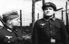 Two men in German WWII uniforms stand by barbed wire, evoking the tense atmosphere of a classic British POW escape drama. This black and white scene captures the style of "Break to Freedom (1953)" DVD.