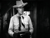 A man in a cowboy hat, neckerchief, and buttoned shirt stands indoors holding an object in this black-and-white image from The Fighting Westerner (1935) DVD, capturing the classic Western film style.