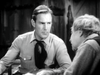 A man in a buttoned-up shirt and neckerchief sits at a table, facing an older man. The rustic scene is from "The Fighting Westerner (1935) DVD" starring Randolph Scott—ideal for classic movie collectors.