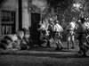 Five uniformed soldiers approach a sandbagged building, one wielding a battering ram. An American flag is seen in this black-and-white World War II film scene. Now available on Suicide Battalion (1958) DVD.